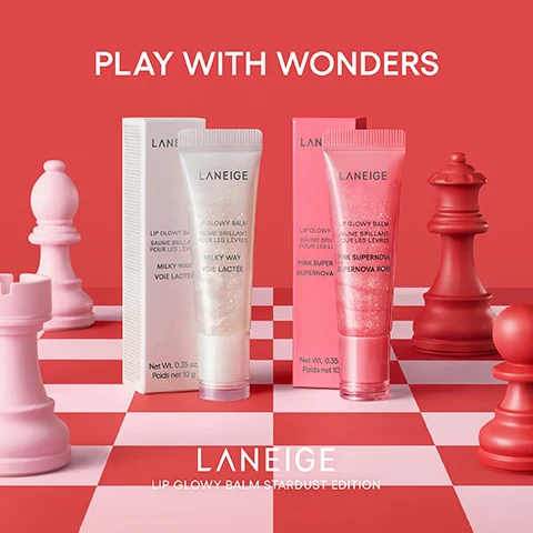 The image shows two Laneige Lip Glowy Balms, one shimmery white labeled Milky Way and one shimmery pink labeled Pink Supernova, standing with their respective boxes on a red and pink checkered surface surrounded by oversized red and pink chess pieces, with the visible text PLAY WITH WONDERS LANEIGE LIP GLOWY BALM BAUME BRILLANT POUR LES LEVRES MILKY WAY VOIE LACTEE Net Wt. 0.35 oz. Poids net 10 g PINK SUPER SUPERNOVA SUPERNOVA ROSE Net Wt. 0.35 Poids net 10 LANEIGE LIP GLOWY BALM STARDUST EDITION.